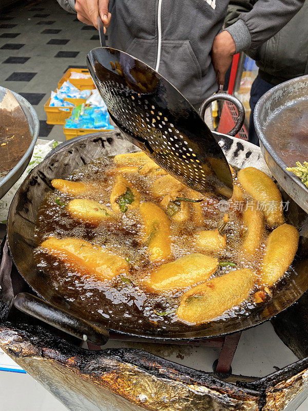 一个不认识的人在煮绿辣椒油饼(mirch pakora)，在大油锅里油炸，印度街头小吃摊贩，印度街头小吃摊档，不健康的饮食，高架视野，重点在前景